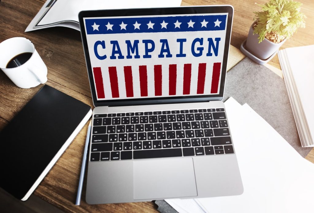Laptop displaying 'Campaign' with American flag design on a desk with coffee and notepad.