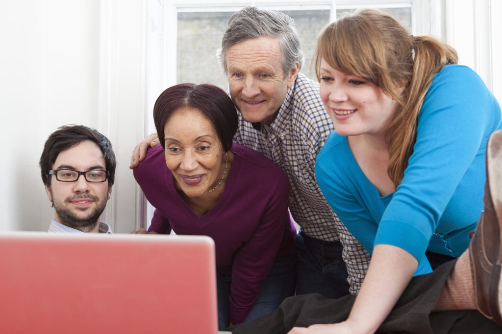 Group of four people smiling and using a laptop together indoors.