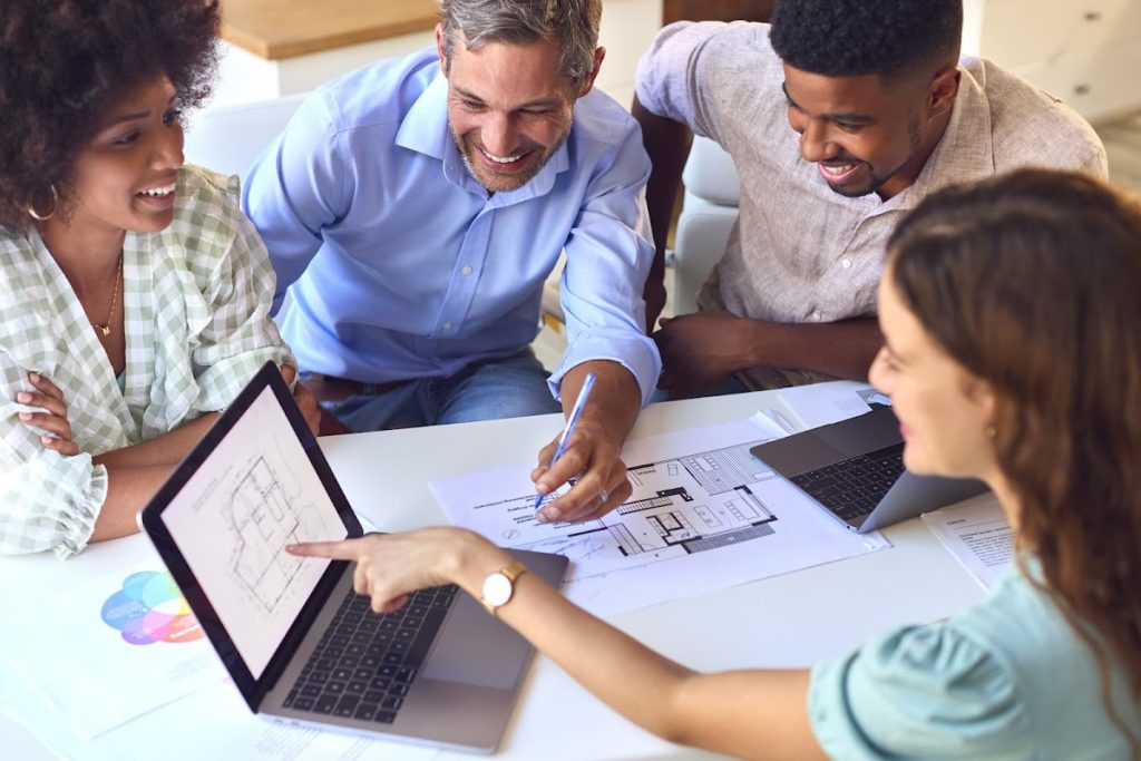 Diverse architects collaborating over blueprints with laptops at a meeting.