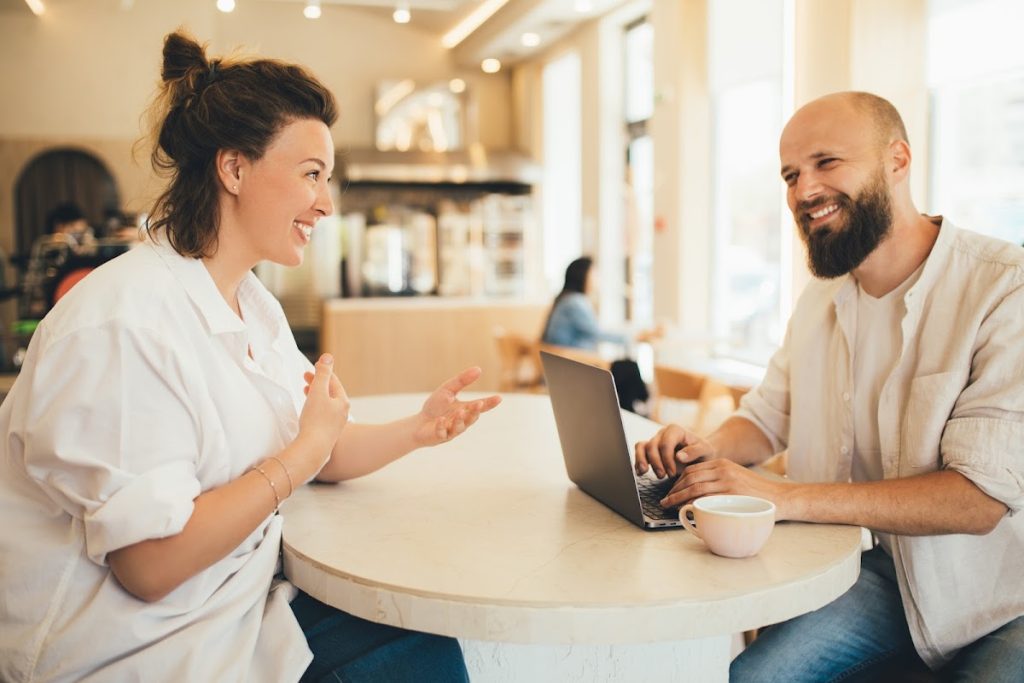 Millennial man and woman in lively discussion over a business project at a cafe table with a laptop.