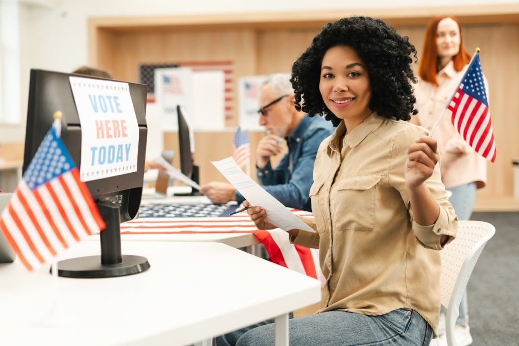 African American woman holding an American flag in a voting booth setting.