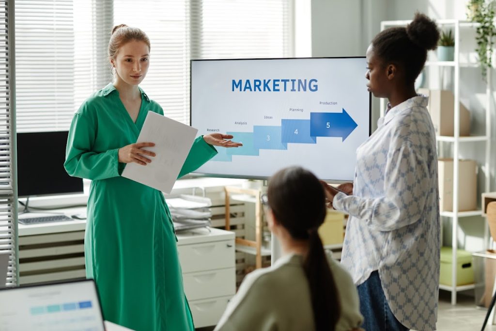 A professional woman giving a business presentation to colleagues in a modern office setting.