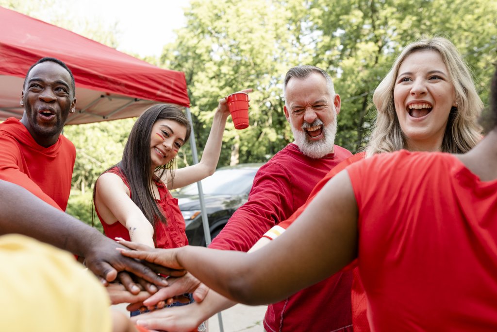 Group of enthusiastic sports fans in red attire huddled together at an outdoor tailgate event.