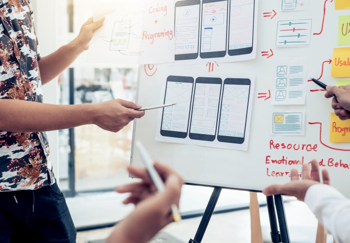 Team designing mobile app wireframes on whiteboard