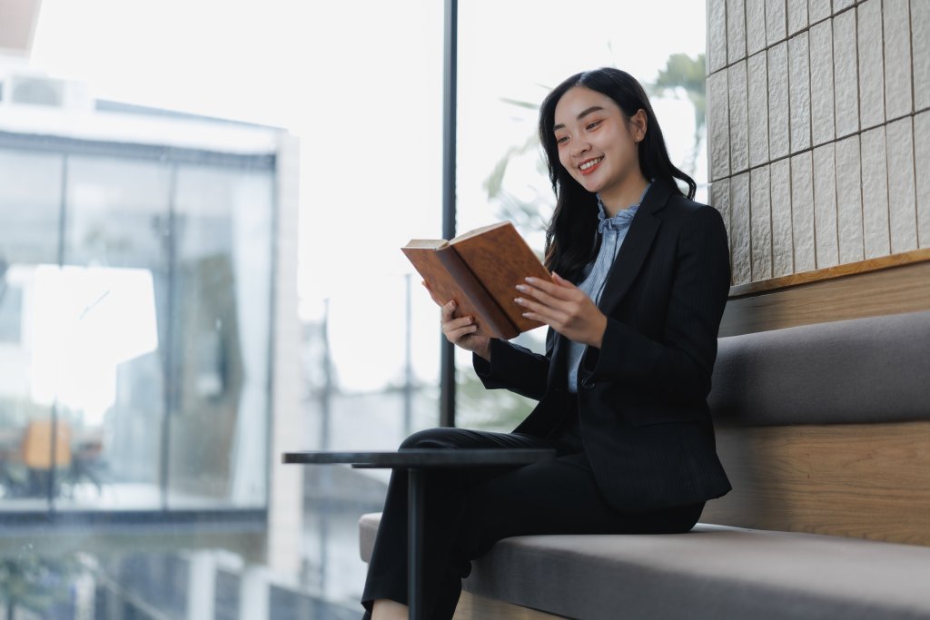 Businesswoman reading book on bench indoors